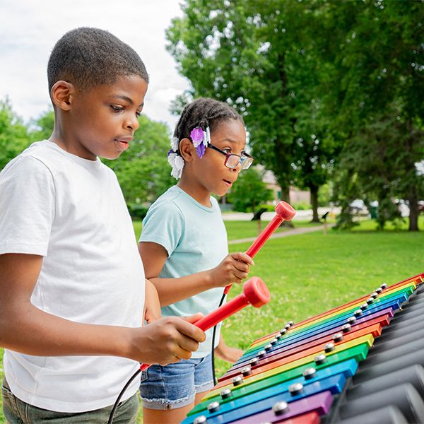 two children playing a large outdoor xylophone in rainbow colors