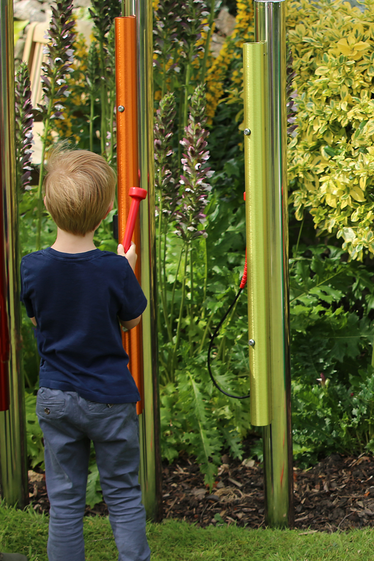 a young boy playing rainbow coloured musical chimes in a school playground