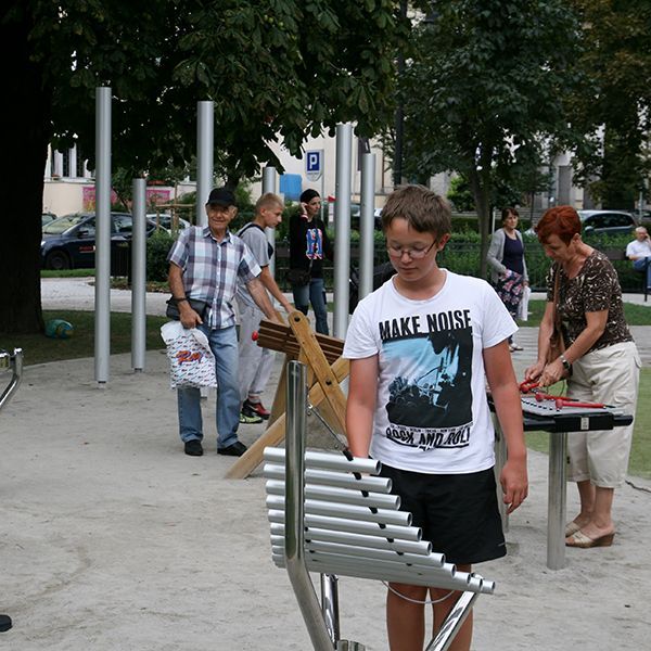 boy in a park playing an outdoor xylophone with other outdoor instruments in the background