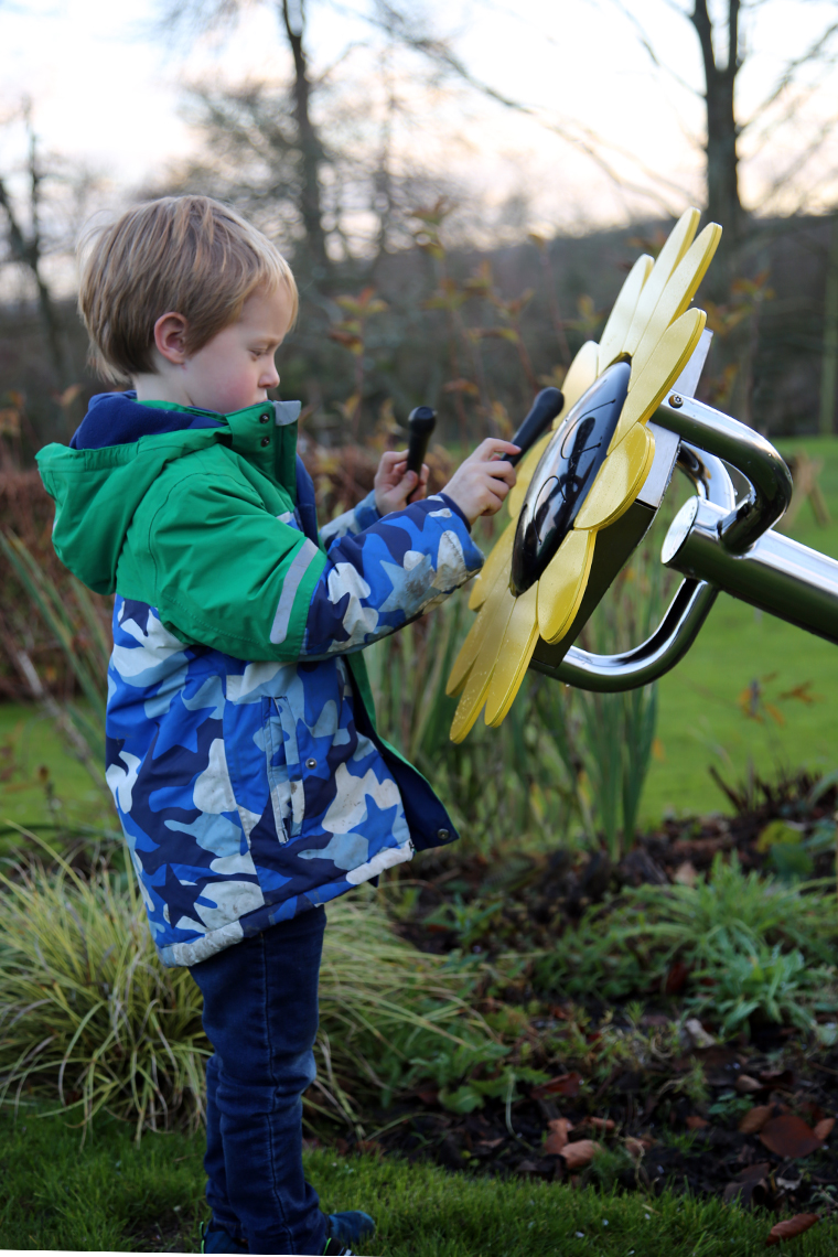 A young boy playing an outdoor musical drum in the shape and colours of a sunflower