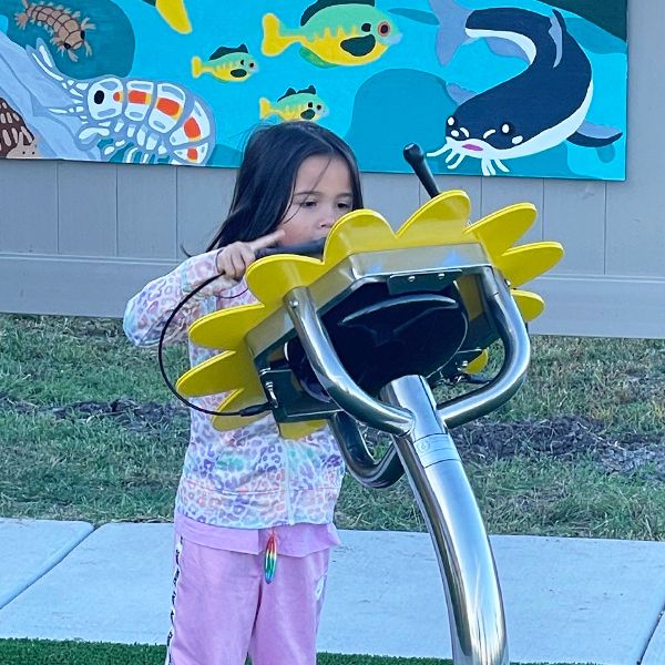 a young girl playing an outdoor drum shaped like a large sunflower in the Kansas Wetlands Center new musical garden