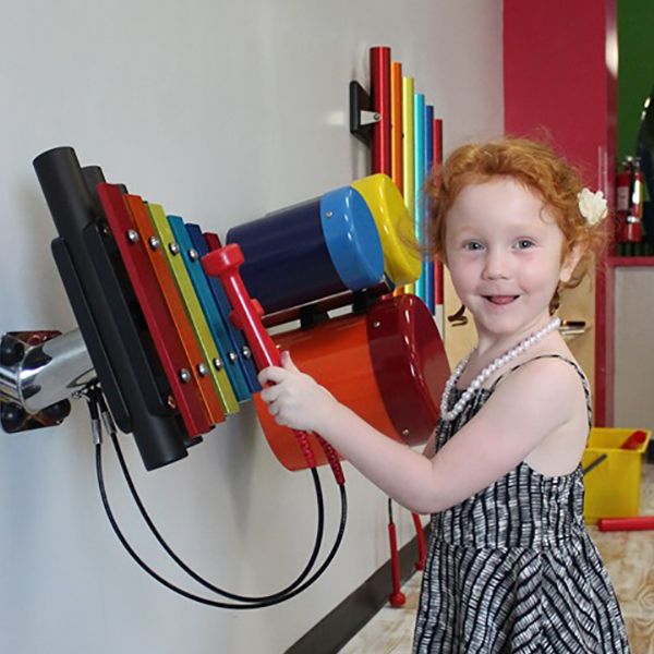 young red-headed girl playing the rainbow coloured xylophone in the building for kids children's museum