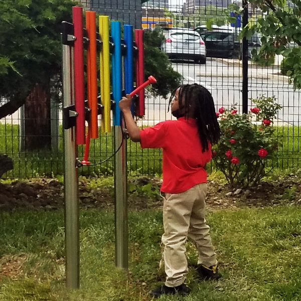 young school boy playing some rainbow colored outdoor musical chimes in the Lift For Life Acaddemy school yard