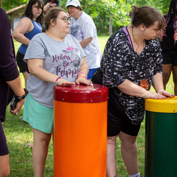 two teenage girls with additional needs playing on outdoor drums in a percussion park at summer camp