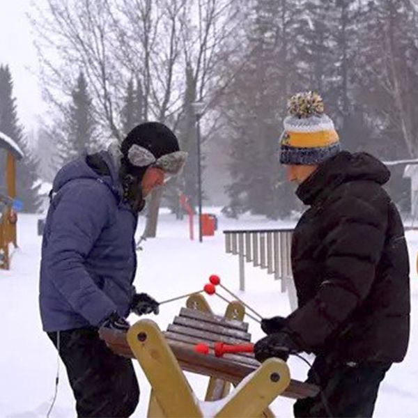 two men playing a large wooden outdoor marimba in the snow