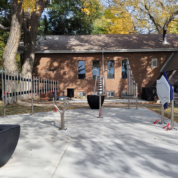 Outdoor musical playground equipment in front of a brick library, surrounded by trees with autumn leaves.