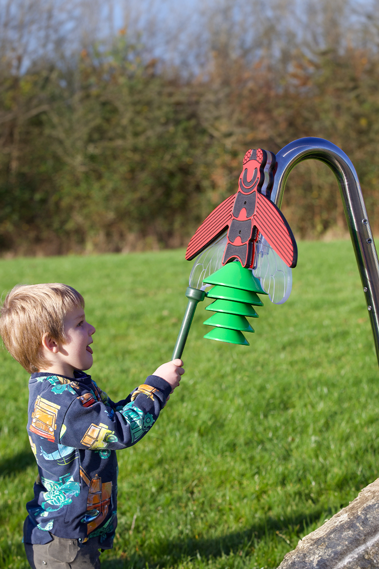 image of a young boy playing an outdoor musical instrument shaped like a firefly on a stainless steel post