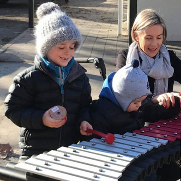 a family of three including a boy in a wheelchair playing on an outdoor xylophone in an inclusive playground