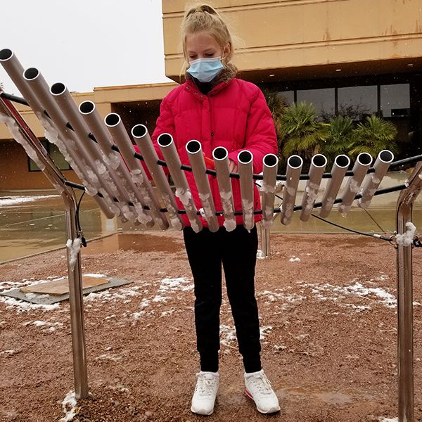 A schoolgirl wearing a red uniform playing an outdoor musical instrument in the school playground