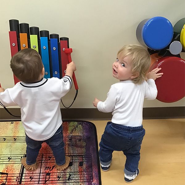 two very young children playing on wall mounted rainbow coloured musical intruments in their nursery school