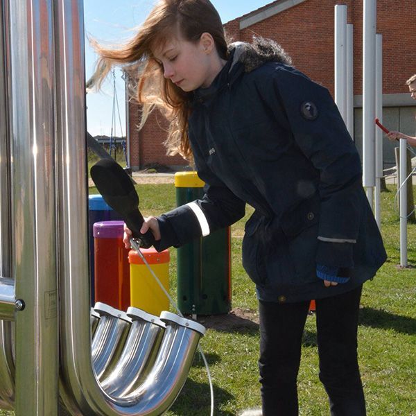 Girl hitting pipes of a large Aerophones with a black paddle in a School Playground