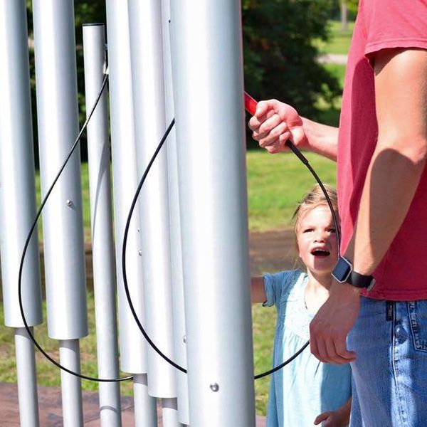 little girl and her father playing the tubular bells outdoor chimes in the st feriole memorial gardens music park