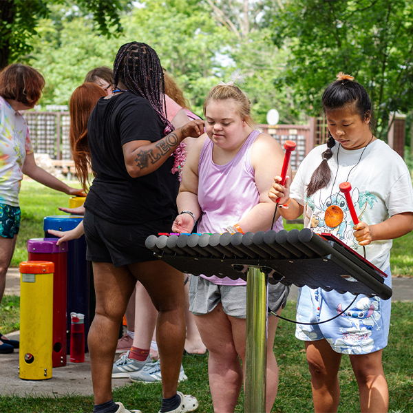 two teenage girls with additional needs playing an outdoor xylophone in a percussion park at summer camp