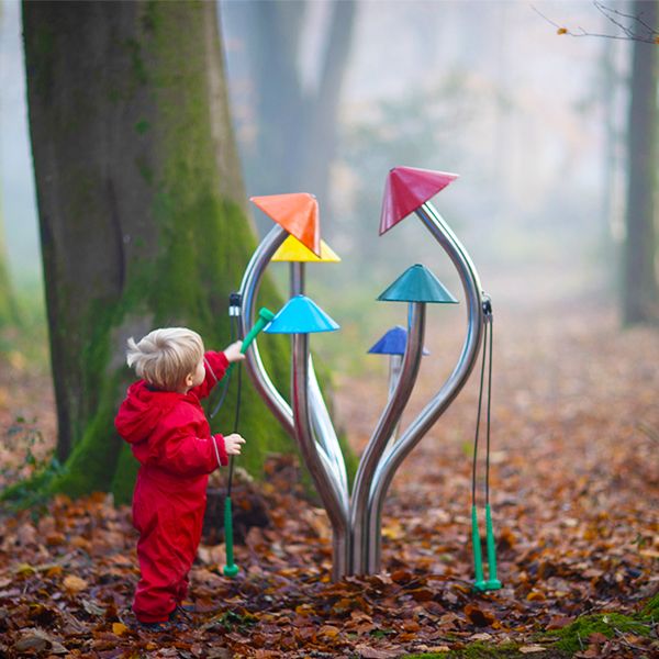 a young boy in a red rainsuit playing outdoor musical chimes shaped like a cluster of colorful mushrooms