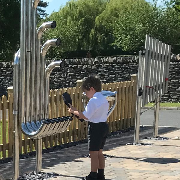 a young boy in school uniform playing a large outdoor musical instrument with curled pipes called tembos