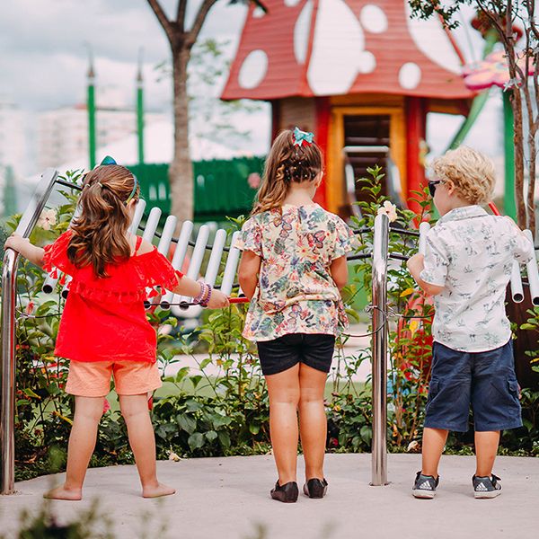 three young children playing a giant silver xylophone in a playground