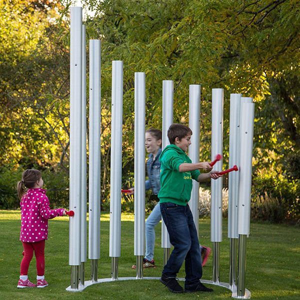 three children running around and hitting huge silver chimes in a playground