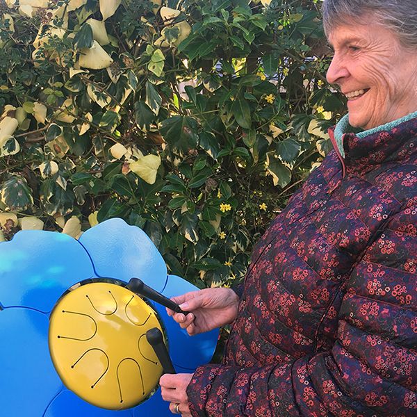 older lady playing a colorful outdoor drum shaped like a forget me not flower in a senior living center