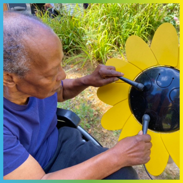 Senior man seated in a wheelchair playing an outdoor musical drum shaped like a sunflower