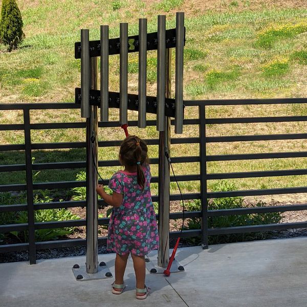 the back of a small child reaching up to play outdoor musical chimes on the children's patio at the scenic regional library