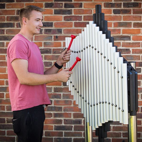 man in a park playing a large metal outdoor xylophone