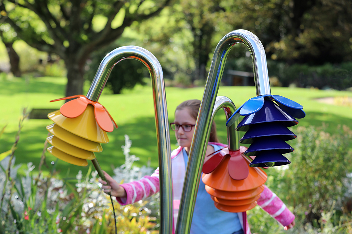 a young girl playing a large outdoor musical instrument with three musical flower heads each in different colours