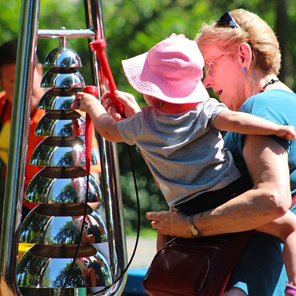 an older lady holding a toddler playing an outdoor bell lyre in the belleville rotary musical garden