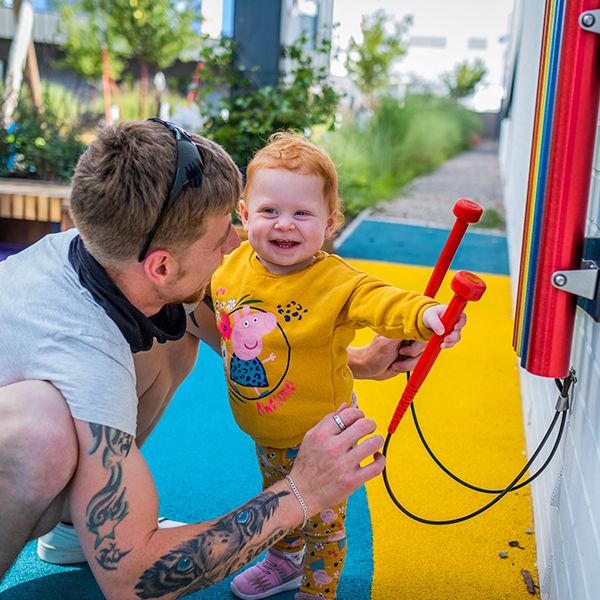 a young red headed girl and her father playing on a set of rainbow colored chimes attached to the wall at the Edinburgh Children's Hospital garden