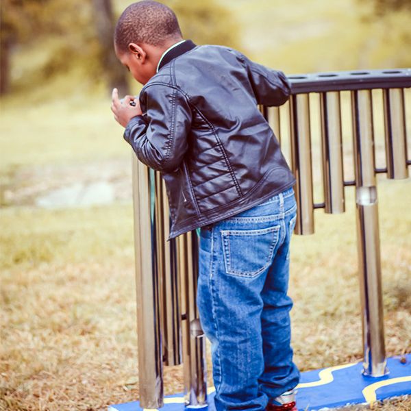 a young boy playing on the outdoor handpipe musical instrument at the Leonel Castillo Community Center 