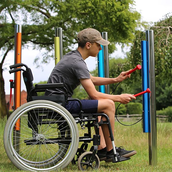 young man in a wheelchair playing rainbow coloured outdoor musical chimes