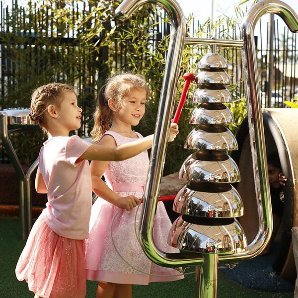 two little girls playing stainless steel bell lyre in shopping precinct playground