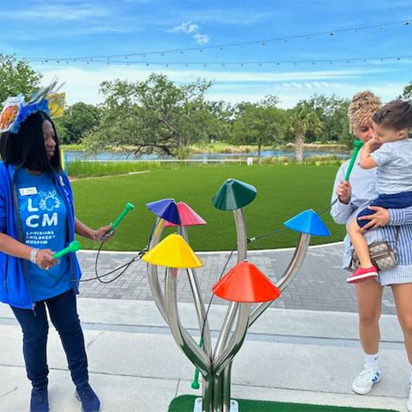 an employee and mother and child playing on an outdoor musical instrument shaped like mushrooms at the Louisiana Children's Museum