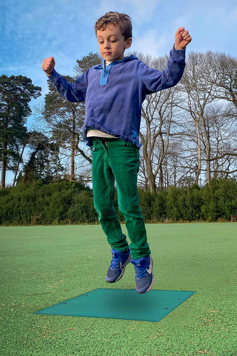 Young boy in a playground jumping onto a square  green outdoor musical chime 