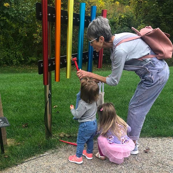 image of an older lady playing on rainbow colored chimes with two children in a library garden