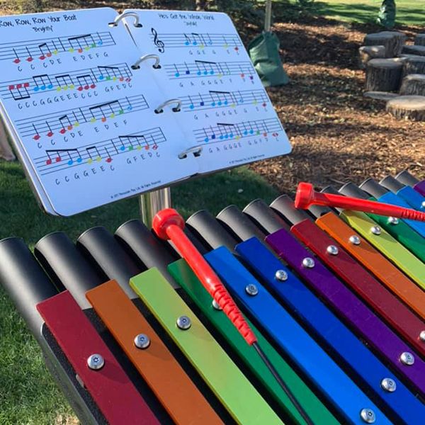 rainbow colored musical notes on an outdoor xylophone with an outdoor music book in the Quinterra Legacy Garden