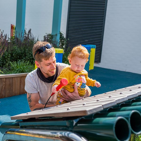 a young red headed girl and her father playing on a large outdoor marimba xylophone at the Edinburgh Children's Hospital garden