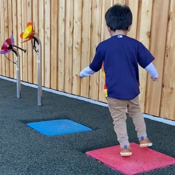 showing the back of a little boy jumping from a red square musical stepping stone to a blue square musical stepping stone in an inclusive playground