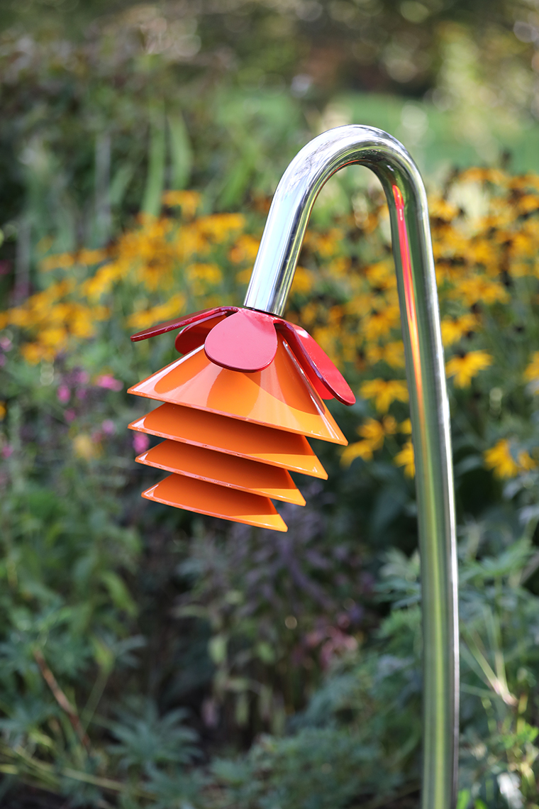 An outdoor musical flower comprising four orange bells and a petal on a stainless steel 'stalk' for playgrounds and sensory gardens