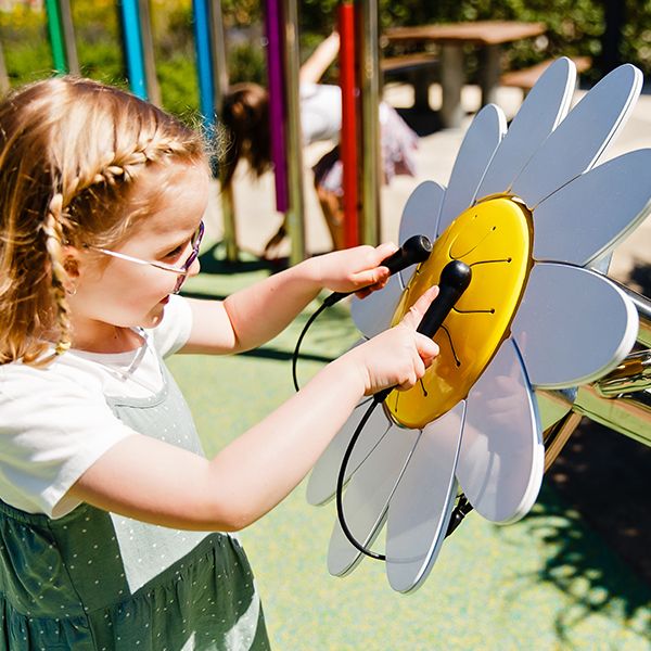 a young girl with glasses playing an outdoor musical drum shaped like a daisy in a musical playground