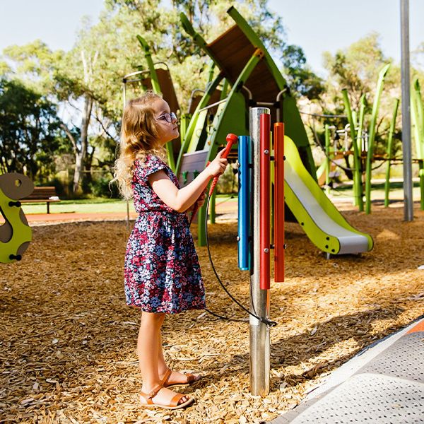 a young girl wearing glasses playing a rainbow colored chimes instrument in a playground