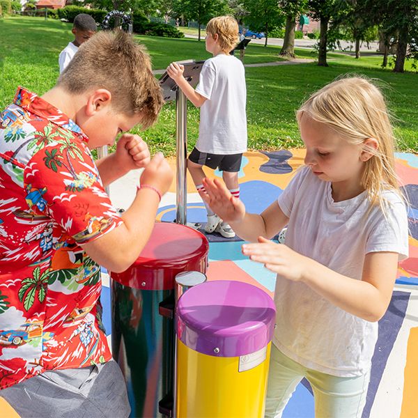 a boy in a floral shirt and a young girl playing colorful outdoor drums in a music park