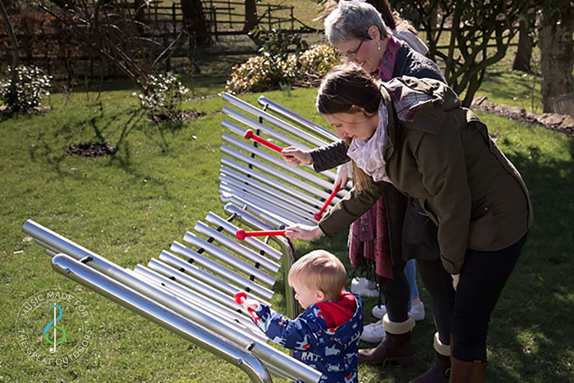 Family playing on large outdoor xylophone together in the park