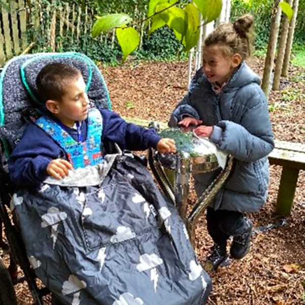 two children, one of which is in a wheelchair, playing a stainless steel tongue drum in a woodland school setting