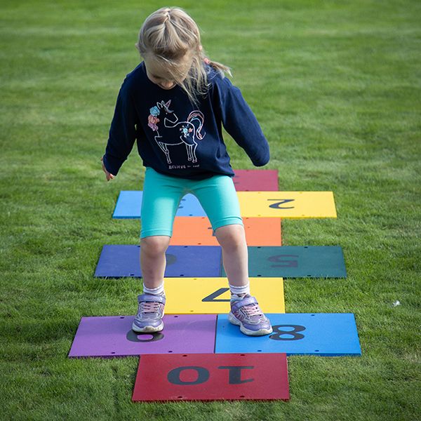 a young girl jumping on an outdoor colourful musical hopscotch installed in grass