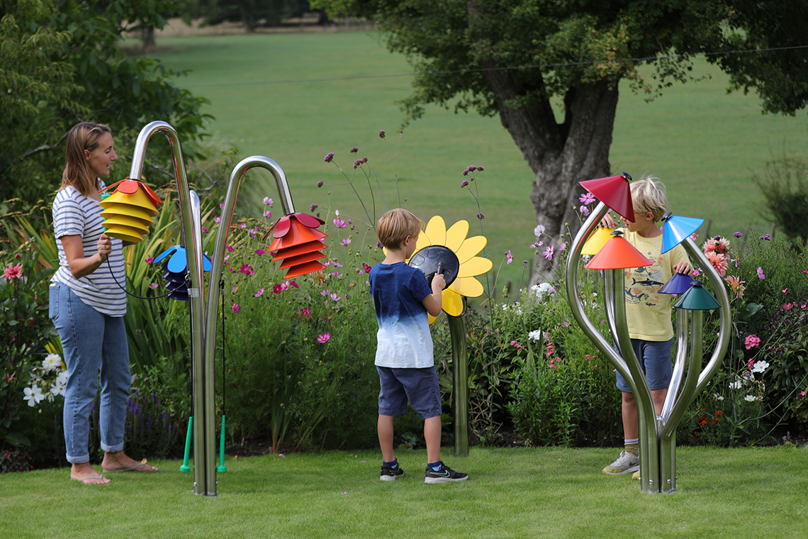 three outdoor musical instruments inspired by nature being played by a mother and two sons