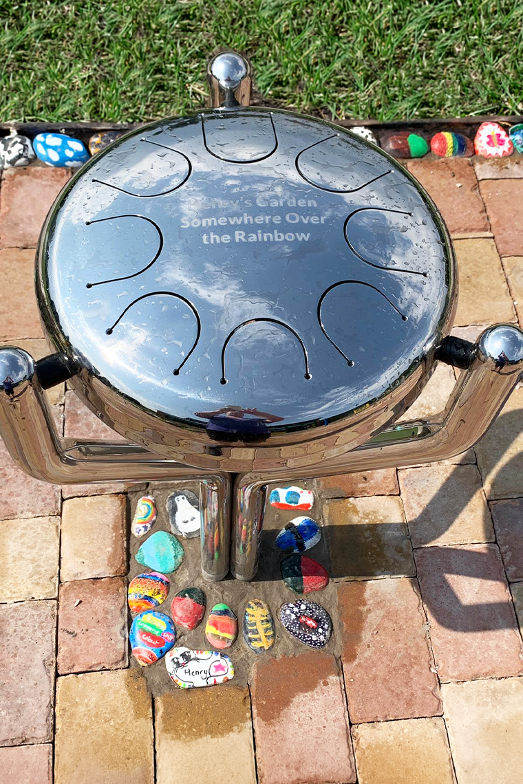 a large silver tongue drum in a memorial garden engraved Henry's Garden Somewhere Over the Rainbow