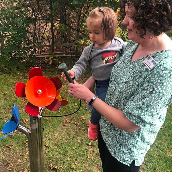 image of a lady holding a baby in her arms and playing an outdoor musical instrument shaped like flowers