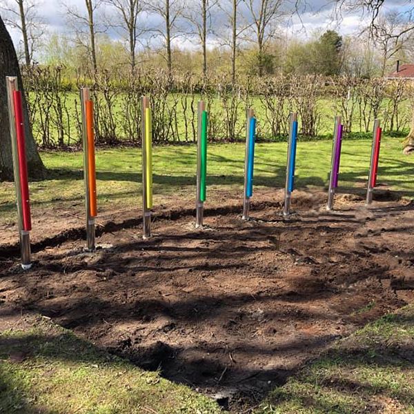 8 colorful outdoor musical chimes installed in the dirt in a school playground