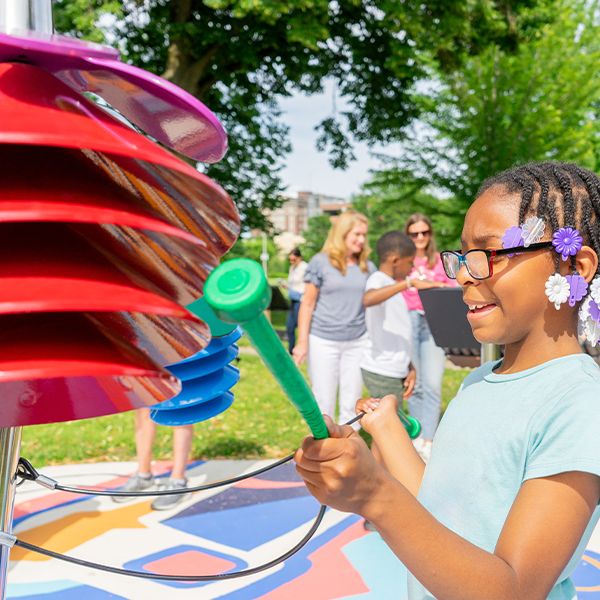 a close up image of a young African american girl playing outdoor musical chimes shaped like flowers in a music park