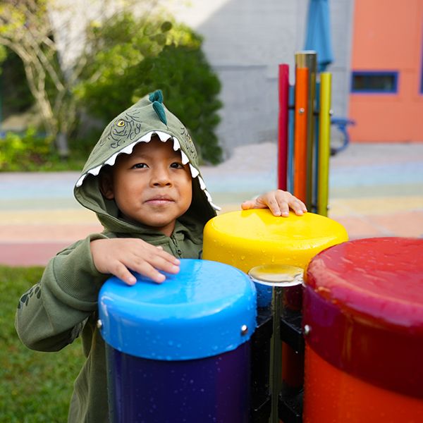 A young boy in a crocodile suit playing a set of bright outdoor drums in a museum sensory garden